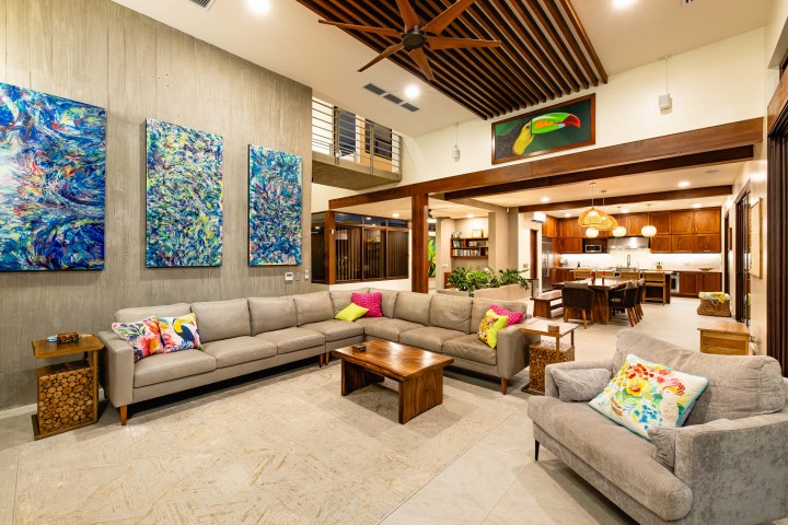 Modern living room with sectional sofa, colorful pillows, abstract art, and view into kitchen.