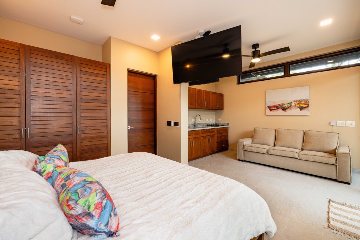 Bedroom with a bed, colorful pillows, sofa, wall-mounted TV, cabinets, and artwork.