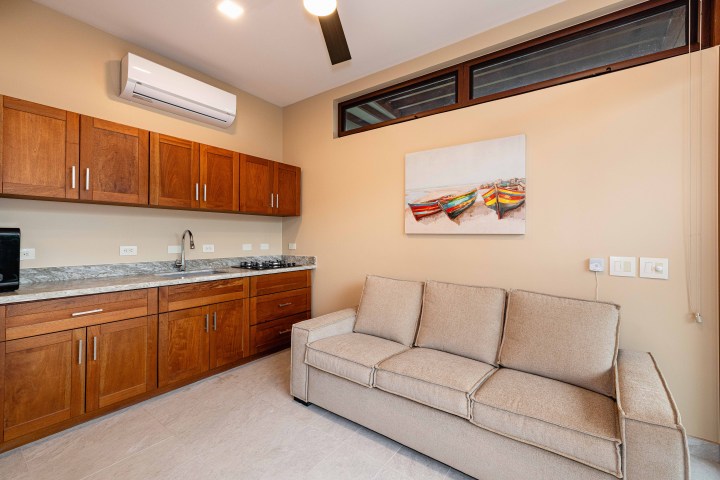 Modern kitchen with wooden cabinets, beige sofa, and painting of colorful boats.