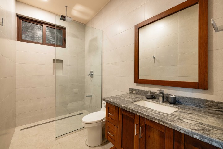 Modern bathroom with wood accents, glass shower, and marble countertop.