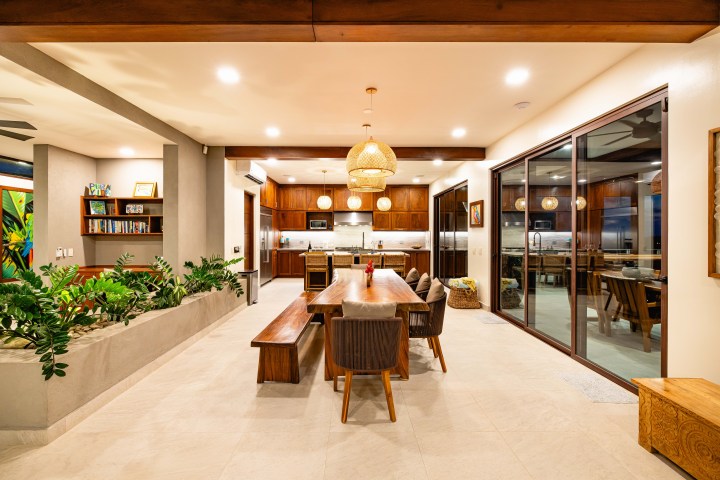 Modern dining area with wooden table, pendant lights, and large glass doors leading to kitchen.