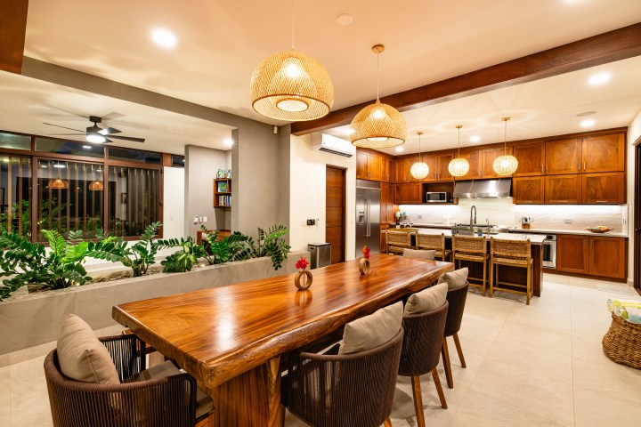 Warm, modern open-plan kitchen and dining area with wooden furniture and pendant lights.