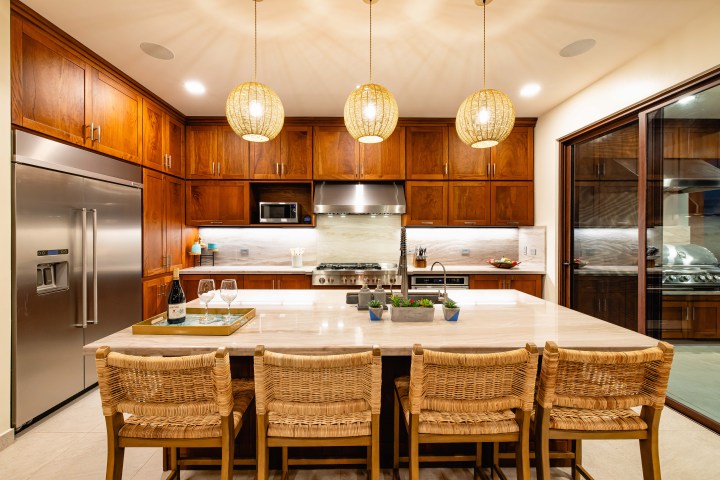 Modern kitchen with wood cabinets, large island with seating, pendant lights, and stainless steel appliances.