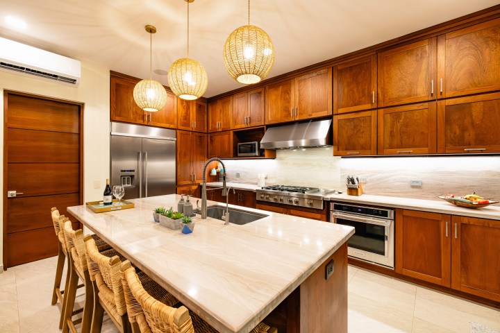 Modern kitchen with wooden cabinets, island, pendant lights, and stainless steel appliances.