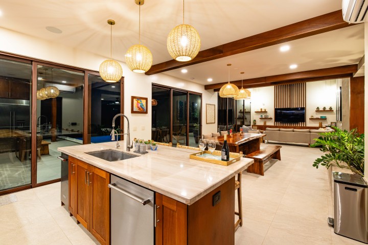 Modern kitchen and living space with wooden island, pendant lights, and glass doors.