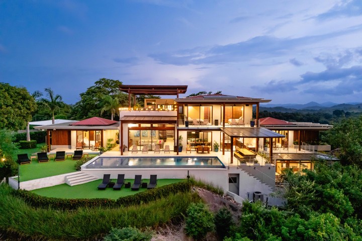 Modern two-story house with large windows and pool at sunset.