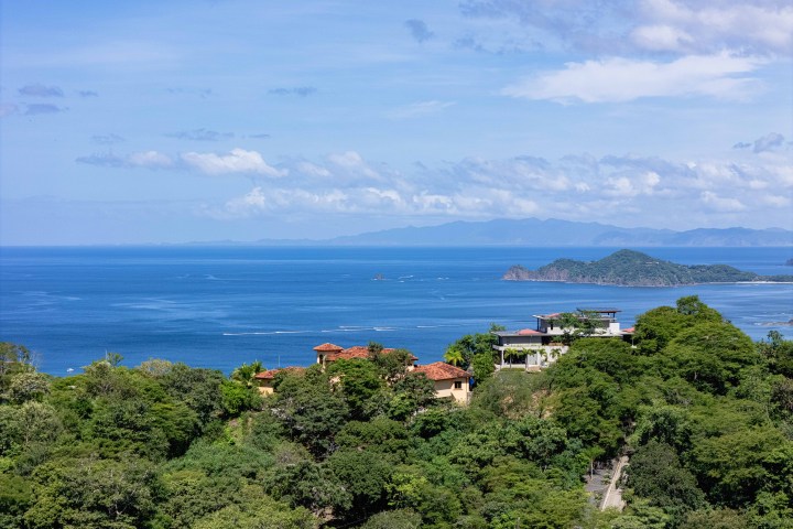 Coastal view with ocean, islands, and buildings nestled in lush green forest.