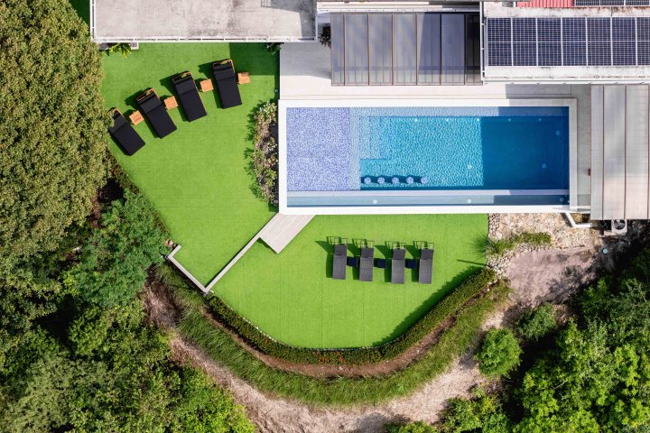 Aerial view of a modern house with pool, sun loungers, and surrounding greenery.