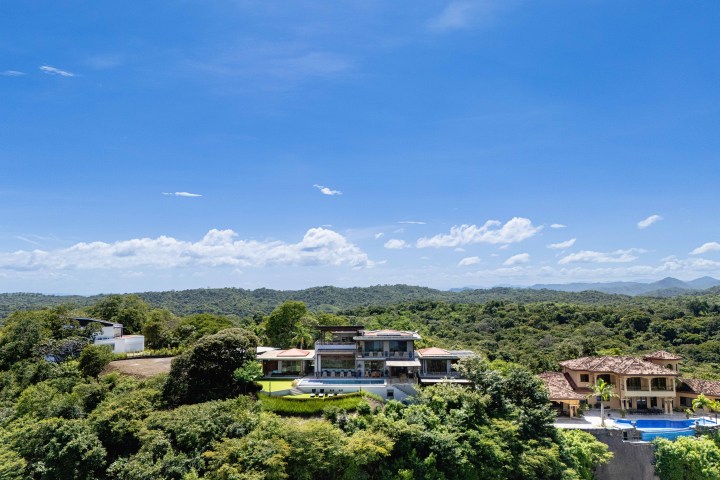 Hilltop modern house with pool surrounded by lush green landscape under a clear blue sky.