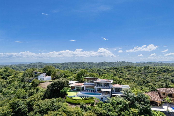 A luxury house with a pool on a lush hillside under a clear blue sky.