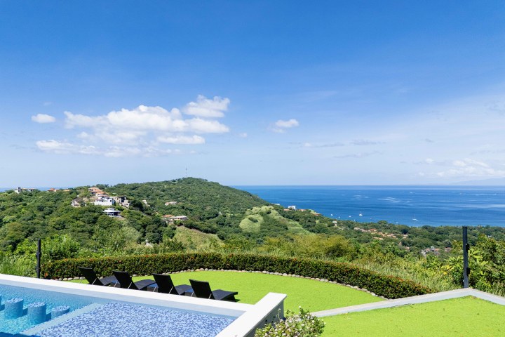 Infinity pool overlooking lush hills and ocean under a clear blue sky.