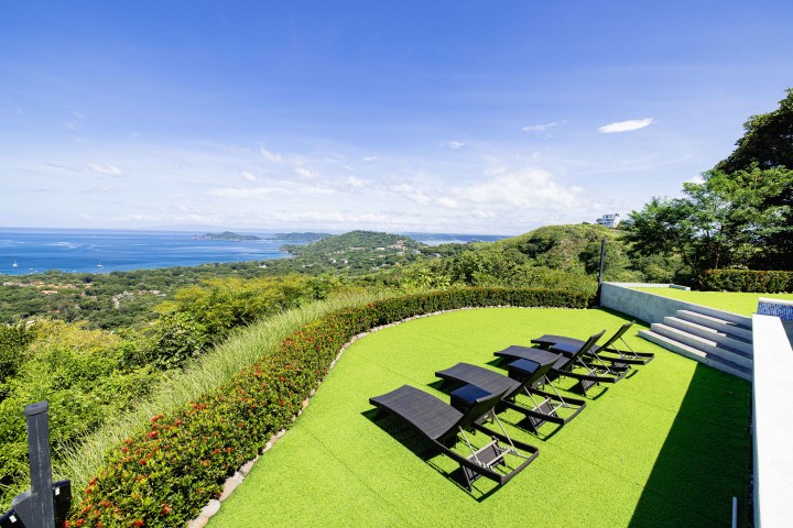 Chairs on a green lawn overlooking a coastal hill with ocean view under a clear blue sky.
