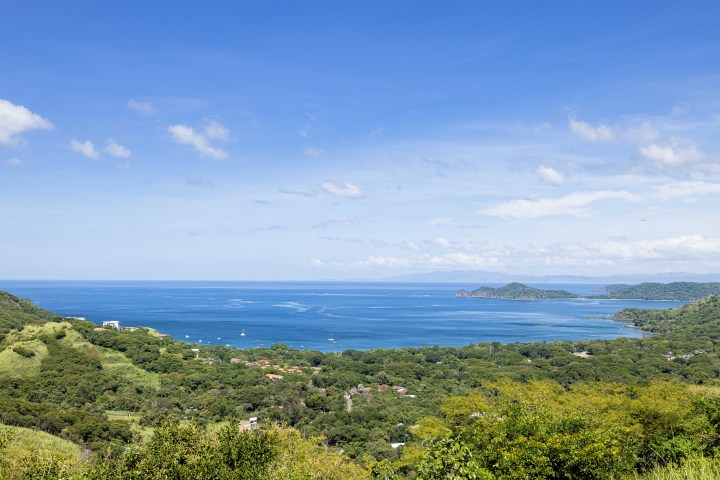 Panoramic view of a lush green coastline with blue ocean and clear sky.
