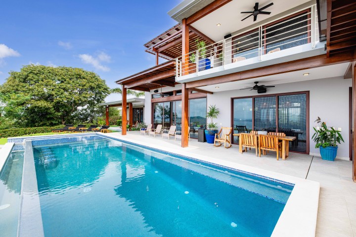Modern house with a pool, patio furniture, and plants under a blue sky.