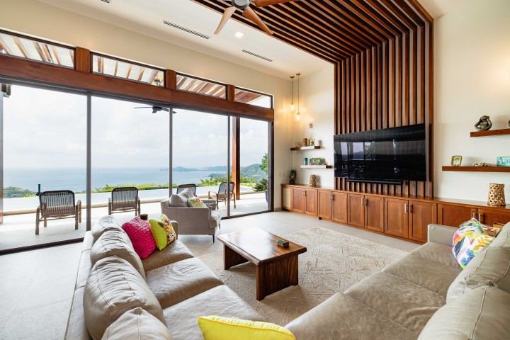 Spacious living room with ocean view, large sofa, TV, and wooden ceiling design.