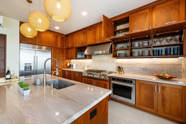 Modern kitchen with wooden cabinets, center island, pendant lights, and stainless steel appliances.