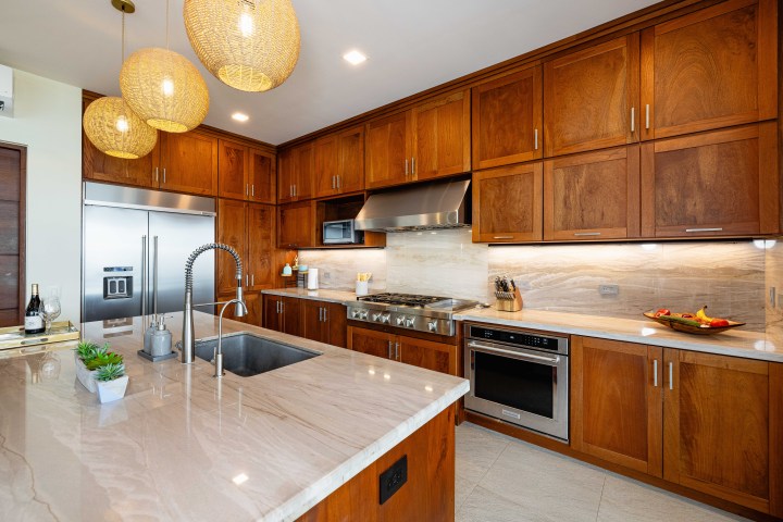 Modern kitchen with wooden cabinets, island sink, pendant lights, and stainless steel appliances.