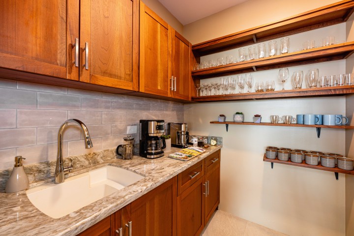 Cozy kitchen nook with wooden cabinets, coffee maker, and shelves of mugs and glasses.