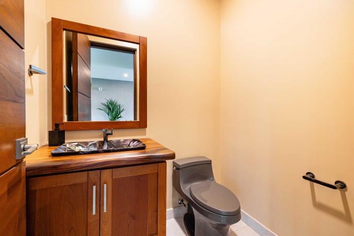 Bathroom with wooden vanity, mirror, gray toilet, beige walls, and towel holder.