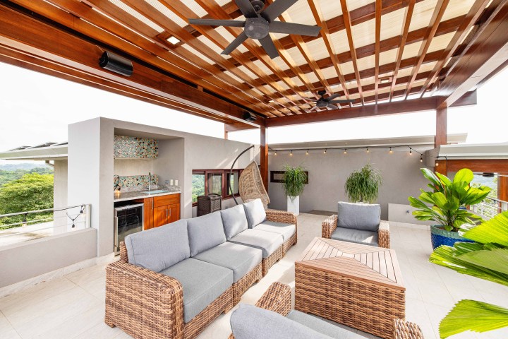 Outdoor terrace with wicker furniture, ceiling fans, and plants under a wooden pergola.