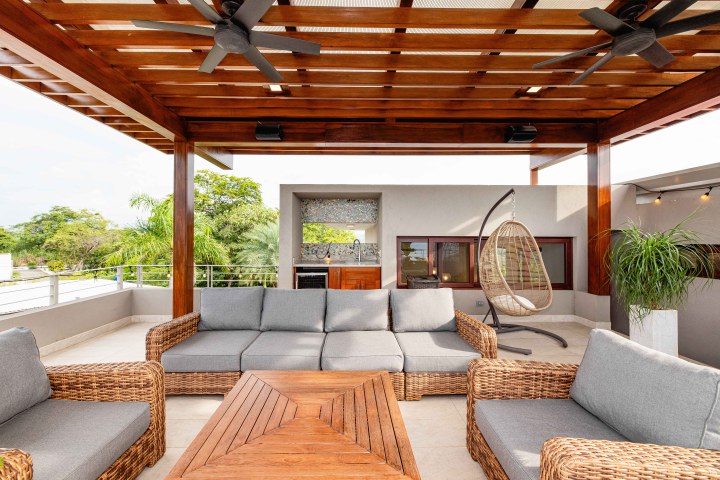Outdoor patio with wicker furniture, pergola, and hanging chair.