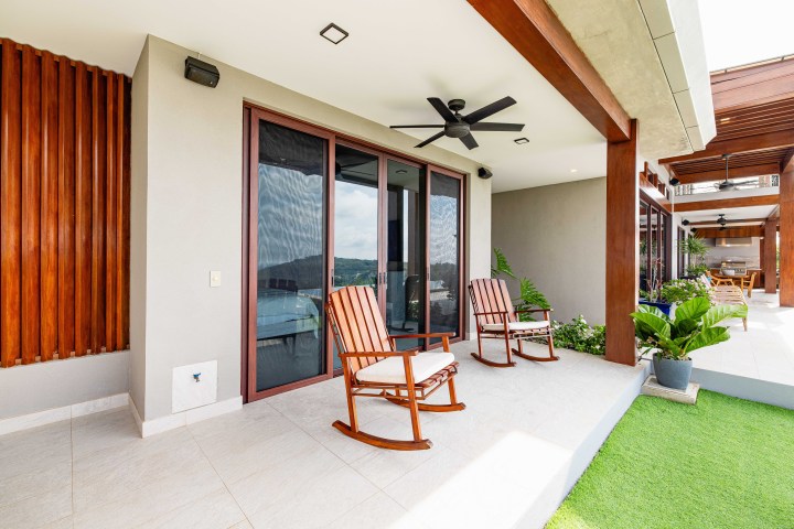 Patio with two rocking chairs, ceiling fan, and sliding glass doors leading to a modern interior.
