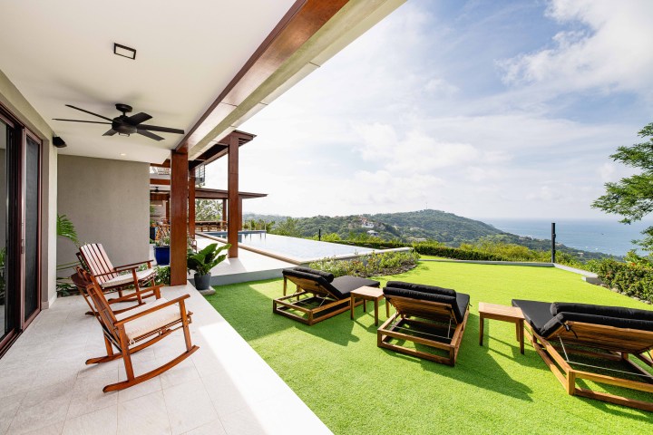 Outdoor patio with rocking chairs, loungers, and ocean view under a sunny sky.