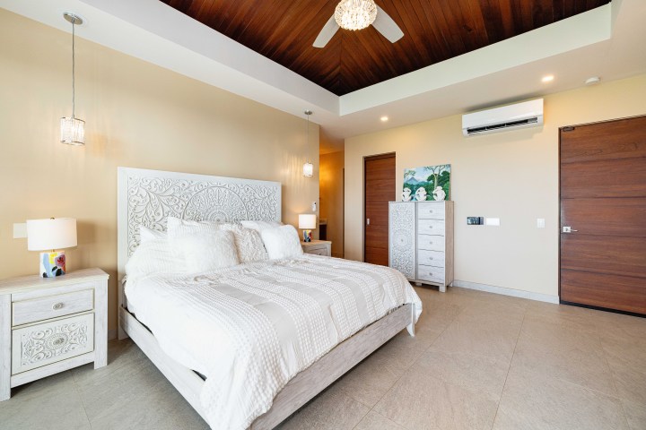 Modern bedroom with a carved bed frame, white bedding, wood ceiling, and decorative dresser.