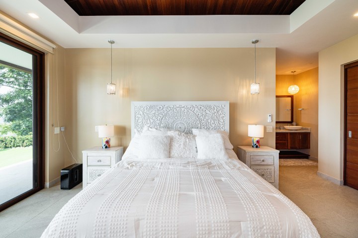 A bright bedroom with a patterned headboard, nightstands, and hanging lights.