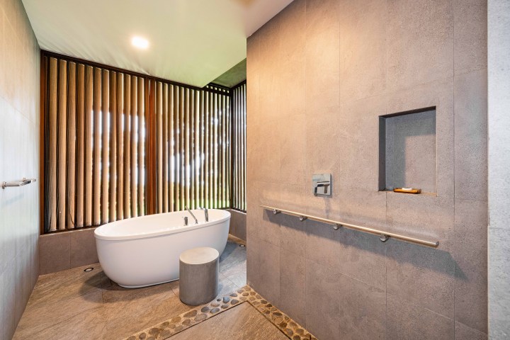 Modern bathroom with freestanding tub, stone stool, and wooden blinds.