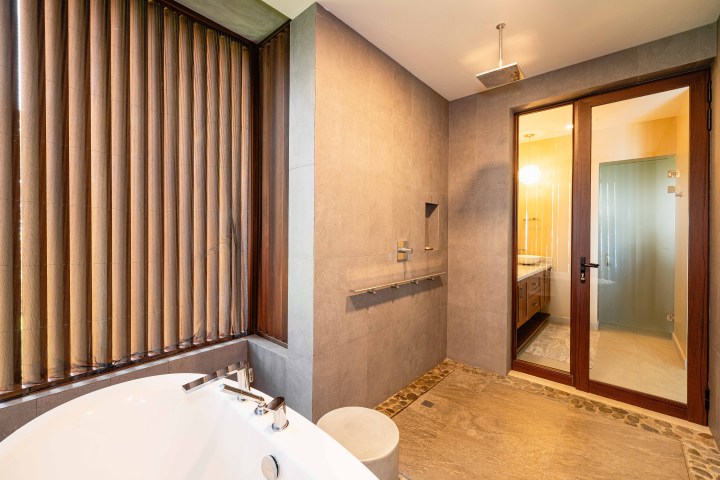 Modern bathroom with bathtub, vertical blinds, and glass door to vanity area.