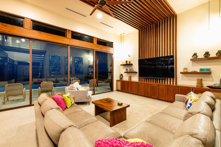Modern living room with beige couches, wooden accents, and large TV.