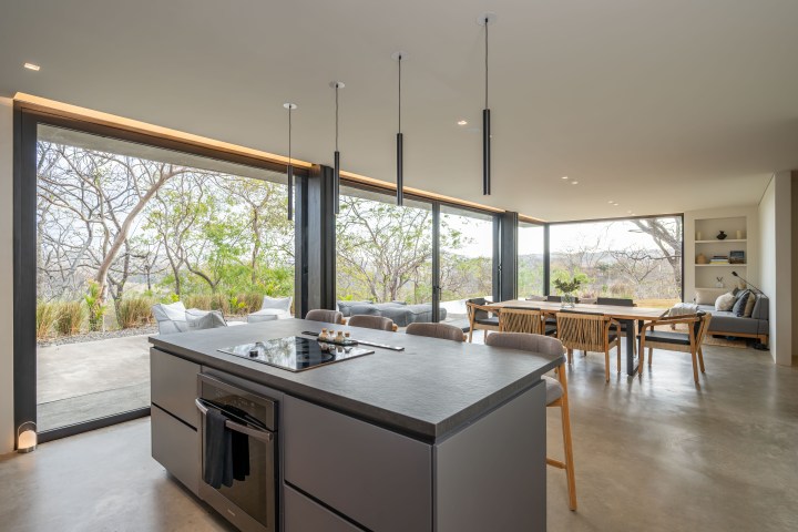 Modern kitchen and dining area with large windows overlooking a patio and trees.