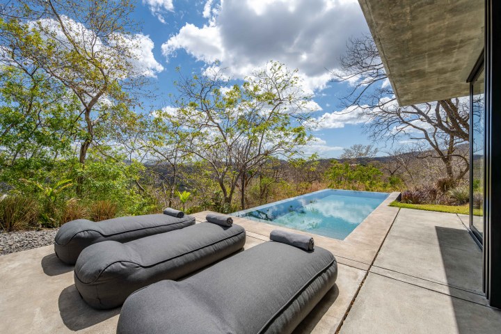 Two gray loungers near an infinity pool overlooking a scenic landscape with trees and clouds.