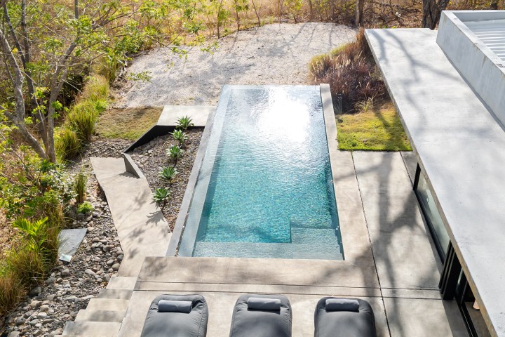 Aerial view of a modern pool with three pool loungers and surrounding trees.
