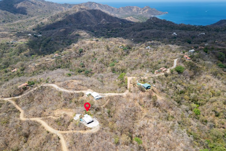 Aerial view of hilly landscape with scattered houses and a red map marker.