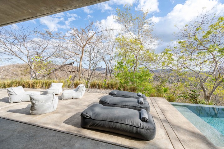 Outdoor patio with gray bean bags, chairs, and pool, overlooking a scenic valley and trees.