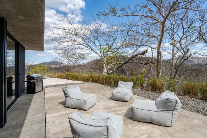 Patio with four gray bean bag chairs and a grill, overlooking a scenic mountain view.