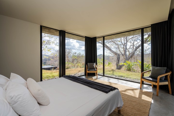 Minimalist bedroom with large windows showing a scenic outdoor view and two chairs beside them.