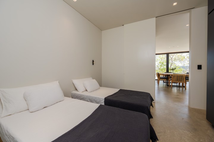 Minimalist room with two single beds and a view of a dining area.