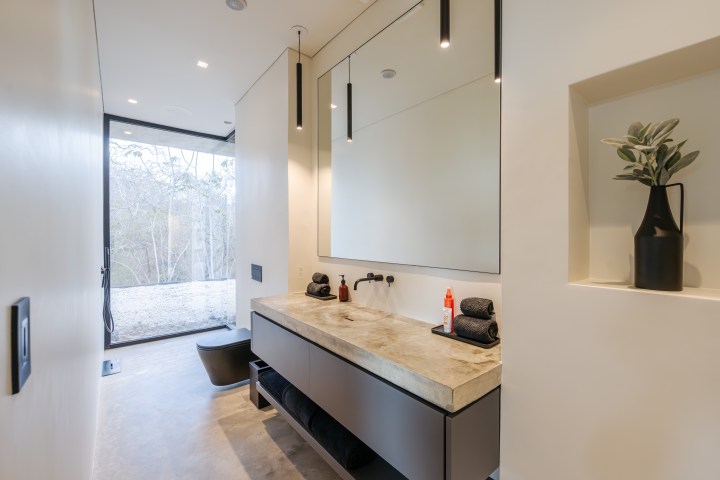 Modern minimalist bathroom with large mirror, concrete sink, and outdoor view.