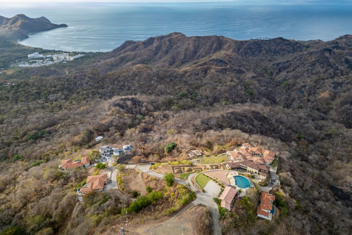 Aerial view of coastal hills, villas, and ocean in the background.