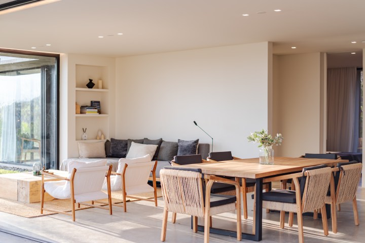 Modern living and dining area with wooden furniture, large windows, and neutral tones.