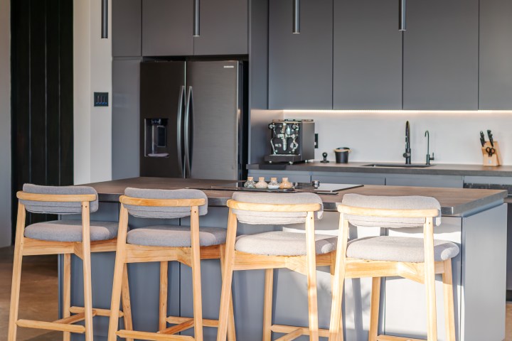 Modern kitchen with gray cabinets, island, wooden stools, and pendant lights.