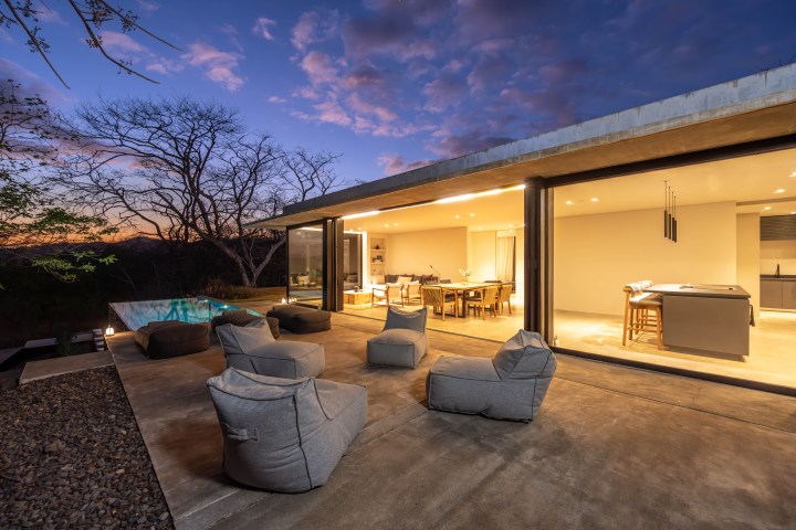 Modern house with open patio, bean bags, and pool at sunset.