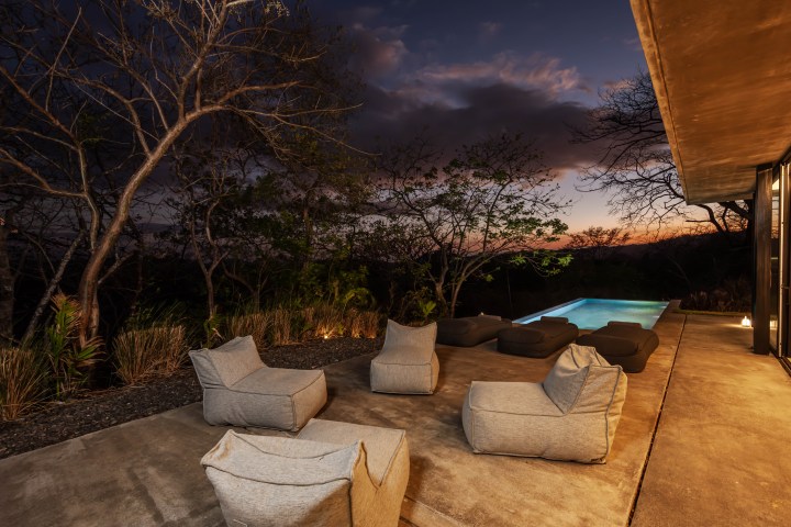 Outdoor patio with bean bag chairs and a pool at sunset, surrounded by trees.