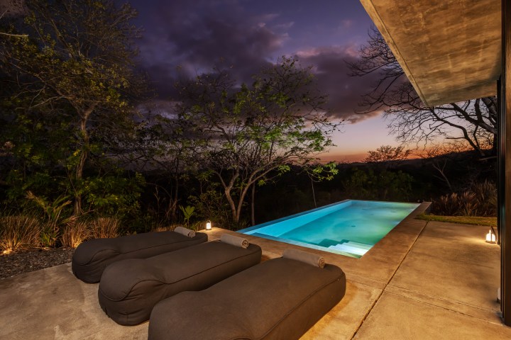 Outdoor pool with lounge chairs at sunset, surrounded by trees.