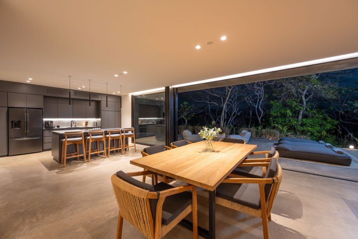Modern kitchen and dining area with outdoor view, large wooden table, and black kitchen island with bar stools.