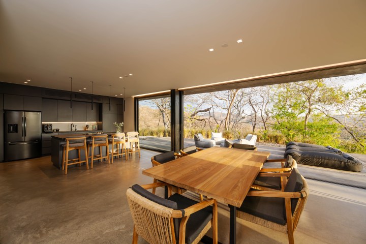 Open-plan kitchen and dining area with large sliding glass doors to patio with outdoor seating and trees.
