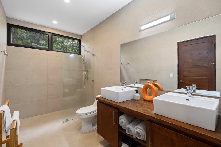 Modern bathroom with glass shower, double sinks, large mirror, and wooden vanity.